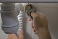 A man repairs plumbing under the sink unscrews the nut fixing the flexible eyeliner for supplying water to the mixer