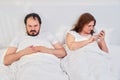 Man resents a woman lying in a white bed. Couple dissatisfied in the bedroom. Quarantine family problems due to coronavirus