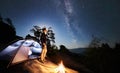 Man resting beside camp, bonfire and tourist tent at night