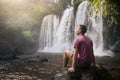 Man resting on stone in front of high waterfall
