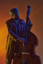 Man in retro flat cap playing double bass with vibrant blue and orange neon light against gradient background.