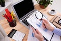 A man review the charts and works with a laptop on his desktop with calculator, pens, pencils, card, phone and a plant Royalty Free Stock Photo