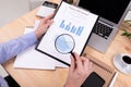 A man review the charts and works with a laptop on his desktop with calculator, pens, pencils, card, phone and a plant Royalty Free Stock Photo