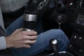 A man rides in a car and holds a thermo mug in his hand
