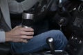 A man rides in a car and holds a thermo mug in his hand