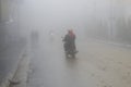 A man rides his motorcycle through dense fog in the city. Royalty Free Stock Photo