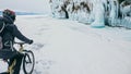 Man is riding bicycle near ice grotto. Rock with ice caves icicl