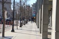 A man riding an electric scooter on the sidewalk with other people walking and cars on the street stopped at a traffic signal