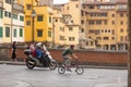 Man riding a motor scooter and a cyclist on the road that runs beside the Arno River