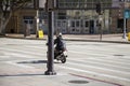 A man riding a tiny motorcycle wearing a backpack surrounded by buildings and traffic signals in Pasadena California