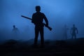 Man with riffle against zombie attack. Zombie apocalypse. Scary view of blurred zombies at cemetery and spooky cloudy sky with fog