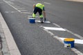 Man road worker applies markings separating bike path from carriageway for cars in city.