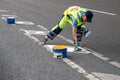 Man road worker applies markings separating bike path from carriageway for cars in city.