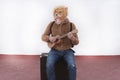 Man with a roaring lion full mask playing ukulele sitting on his briefcase on white background