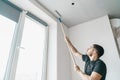 Man with a roller in his hands paints the ceiling in the gray color near the window of his house. Royalty Free Stock Photo