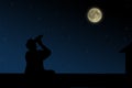 The man on the roof looks through binoculars at the full moon at night.