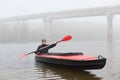 Man rowing in boat on foggy morning, concentrated sportsman enjoying water sport, sitting with paddle in canoe with foggy bridge Royalty Free Stock Photo