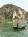 Man rowing boat over emerald water with limestone island in background in summer at Quang Ninh, Vietnam