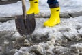 Man in rubber foam boots cleaning the track from old snow. He shovels off dirty wet snow with a shovel so that it melts faster Royalty Free Stock Photo