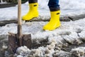 man in rubber foam boots cleaning the track from old snow. He shovels off dirty wet snow with a shovel so that it melts Royalty Free Stock Photo