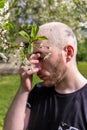 A man rubbing his nose suffering from the seasonal pollen allergy attack standing next to the flowering tree in the spring park. Royalty Free Stock Photo