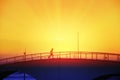 Man running crossing a bridge next to the beack at sunset.