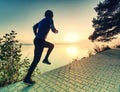 Man running on lake shore pavement during sunrise or sunset