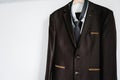 A man`s brown jacket, shirt and tie hangs on a hanger on the background white wall Royalty Free Stock Photo