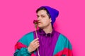 Man in 90s clothes sniffs blossom peony flower on pink background.