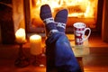 Man`s feet in warm socks with large mug of hot chocolate and murshmallows near fireplace