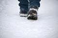 A man\'s feet in winter warm, comfortable shoes take a step on a snowy road in the park on a winter walk.