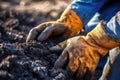 A man\'s gloved hands are picking up biochar to add to the soil in his garden. Biochar increases soil carbon to improve