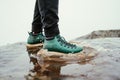 A man`s green boots enter a puddle, close-up photo in motion. Hiker in boots walks on puddles in the mountains