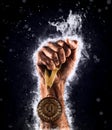 Man`s hand in a blue fire is holding up gold medal. Winner in a competition. Royalty Free Stock Photo