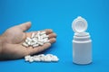 A man`s hand with a bunch of pills and an open white bottle on a blue background. Royalty Free Stock Photo