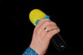 A man\'s hand close-up holds a microphone with a yellow soft rim, a karaoke singing tool on a dark background