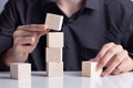 Man`s hand completing set of 4 stacked wooden cubes, man build a tower by using four blank wooden cube on table. Mockup for letter