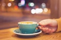 ManÃ¢â¬â¢s hand with cup of coffee in a cafe on a background of city lights behind window. Toned photo Royalty Free Stock Photo