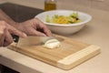 A man`s hand cutting an onion with a knife on top of a wooden board Royalty Free Stock Photo