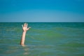 A man`s hand drowns in water calling for help, against the background of the sea and sky clouds summer