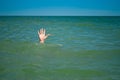 A man`s hand drowns in water calling for help, against the background of the sea and sky clouds summer