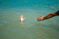 A man`s hand drowns in water calling for help, man helps rescue, against the background of the sea