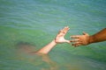 A man`s hand drowns in water calling for help, man helps rescue, against the background of the sea