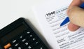 A man\'s hand fills out a 1040 Tax form with a blue pen and calculator Royalty Free Stock Photo