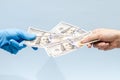 Man`s hand giving money dollars to a hand in blue surgical glove, nurse or doctor. Corruption in medicine field