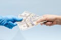 Man`s hand giving money dollars to a hand in blue surgical glove, nurse or doctor. Corruption in medicine field