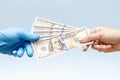 Man's hand giving money (dollars) to hand in blue surgical glove, nurse or doctor. Corruption in medicine field