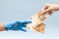 Man's hand giving money (euro) to hand in blue surgical glove, nurse or doctor. Corruption in medicine
