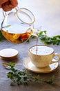 Man`s hand with glass teapot pouring tea into white cup, grey background