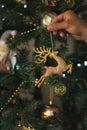 Man`s hand hanging a golden deer on a decorated christmas tree. Close up. Royalty Free Stock Photo